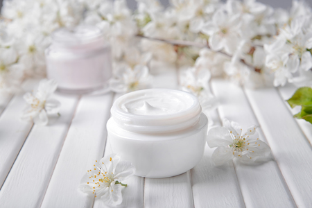 Jar with cream and blooming flowers on tableの写真素材