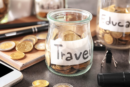Glass jar with savings for travel and coins on tableの写真素材