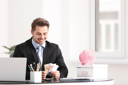 Young businessman counting money at table indoors. Money savings conceptの写真素材