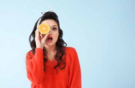 Beautiful young woman with half of orange on color backgroundの写真素材