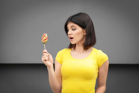 Beautiful young woman with lollipop on grey backgroundの写真素材