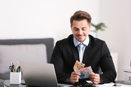 Young businessman counting money at table indoors. Money savings conceptの写真素材