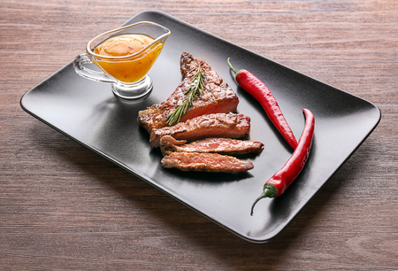 Plate with tasty grilled steak, chili and sauce on wooden tableの写真素材