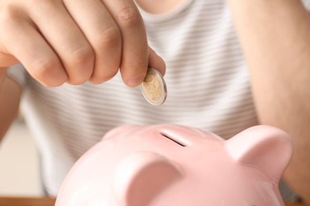 Man putting coin into piggy bank, closeup. Money savings conceptの写真素材