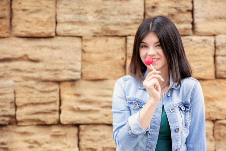 Beautiful young woman with lollipop against brick wallの写真素材