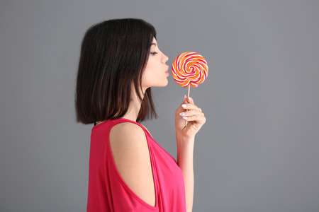 Beautiful young woman with lollipop on grey backgroundの写真素材