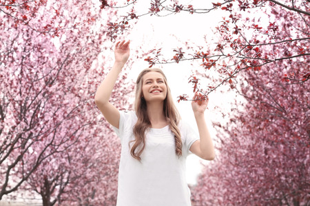 Beautiful young woman near blossoming tree on spring day