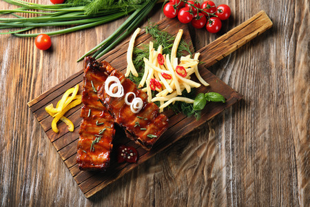 Wooden board with delicious grilled ribs and french fries on tableの写真素材