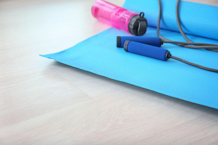 Yoga mat with jumping rope and bottle of water on wooden floor