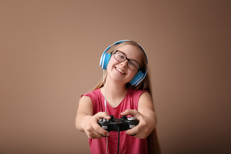 Cute girl with gamepad on color background