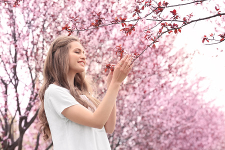 Beautiful young woman near blossoming tree on spring day