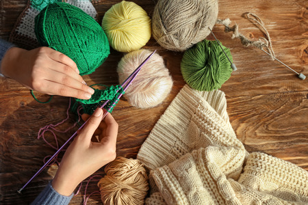 Young woman knitting clothes at table