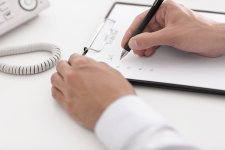 Businessman writing to-do list at table in officeの写真素材