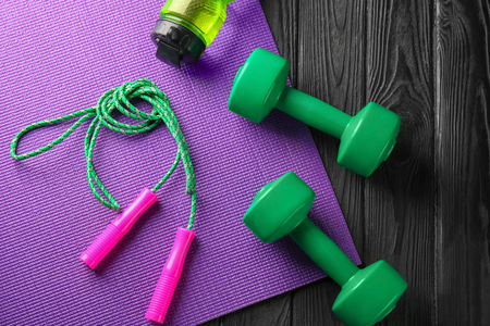 Yoga mat with jump rope and  dumbbells on wooden backgroundの写真素材