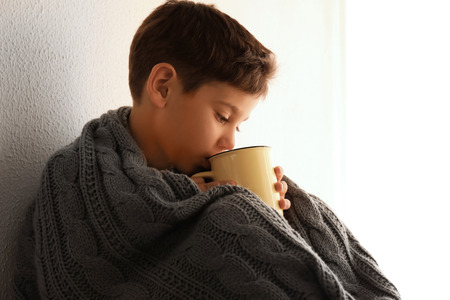 Cute little boy with cup of hot cocoa drink near windowの写真素材