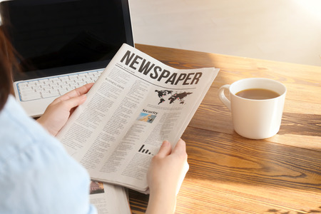 Young woman reading newspaper at table indoors