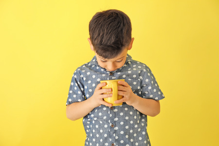 Cute little boy with cup of hot cocoa drink on color backgroundの写真素材