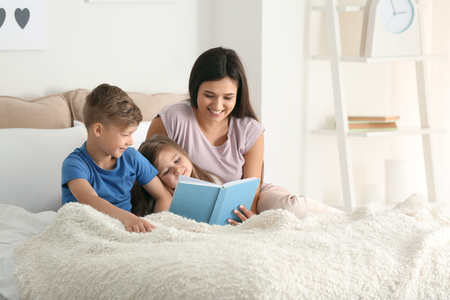 Mother and her children reading book together at homeの写真素材