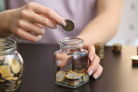 Woman putting coins into glass jar on table. Savings conceptの写真素材