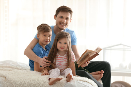 Father and his children reading book together at homeの写真素材