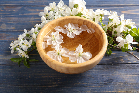Bowl with water and blooming flowers on wooden tableの写真素材