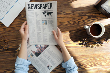 Young woman reading newspaper at tableの写真素材