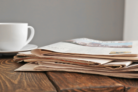Pile of newspapers with cup of tea on wooden tableの写真素材