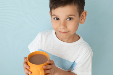 Cute little boy with cup of hot cocoa drink on light backgroundの写真素材