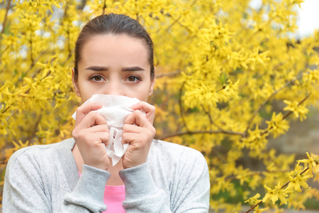 Young woman with nose wiper near blooming tree. Allergy conceptの写真素材