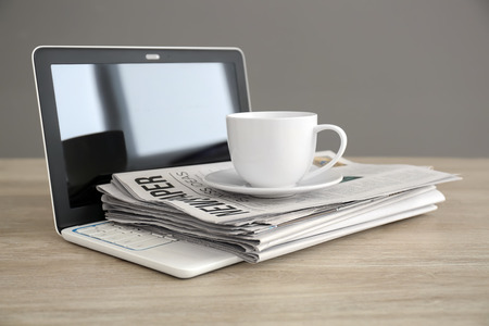 Pile of newspapers, laptop and cup of coffee on wooden tableの写真素材