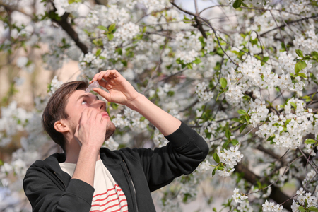 Young man using eye drops near blooming tree. Allergy conceptの写真素材