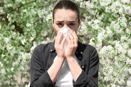Young woman with nose wiper near blooming tree. Allergy conceptの写真素材