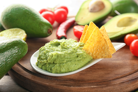 Delicious guacamole with nachos and vegetables on wooden boardの写真素材