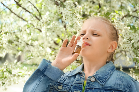 Little girl using nasal drops near blooming tree. Allergy conceptの写真素材