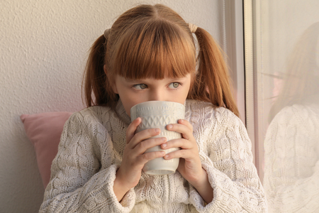 Cute little girl with cup of hot cocoa drink near windowの写真素材
