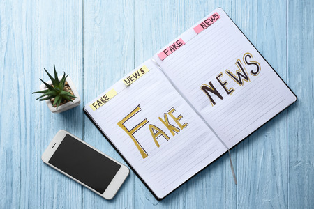 Notebook with words FAKE NEWS and mobile phone on wooden backgroundの写真素材
