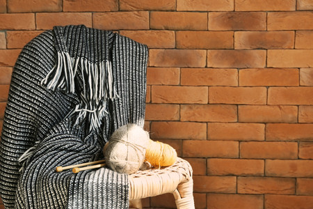 Knitting yarn with needles and plaid on chair near brick wallの写真素材