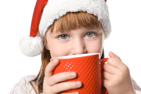 Cute little girl in Santa hat and with cup of hot cocoa drink on white backgroundの写真素材