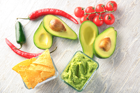 Bowls with delicious guacamole, nachos and vegetables on tableの写真素材