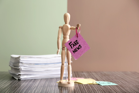 Small human figure holding paper sheet with words FAKE NEWS on wooden tableの写真素材