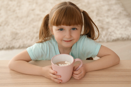 Cute little girl with cup of hot cocoa drink at homeの写真素材