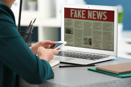 Woman with phone reading news on laptop indoorsの写真素材