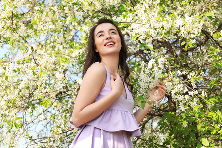 Beautiful young woman near blossoming tree on sunny spring day