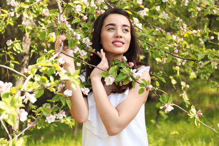 Beautiful young woman near blossoming tree on sunny spring dayの写真素材