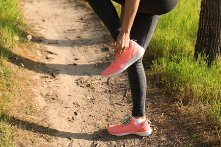 Sporty young woman tying shoelaces before running in park