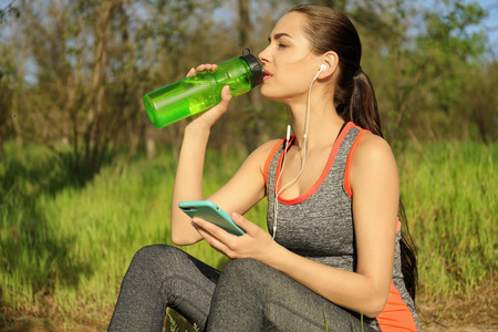 Sporty young woman drinking water after running in parkの写真素材