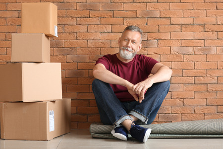 Mature man with moving boxes sitting on carpet at new homeの写真素材