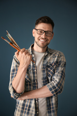 Male artist holding paintbrushes on color backgroundの写真素材