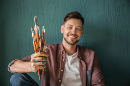 Male artist with paint tools on color backgroundの写真素材
