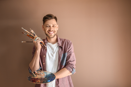 Male artist with paint tools and palette on color backgroundの写真素材